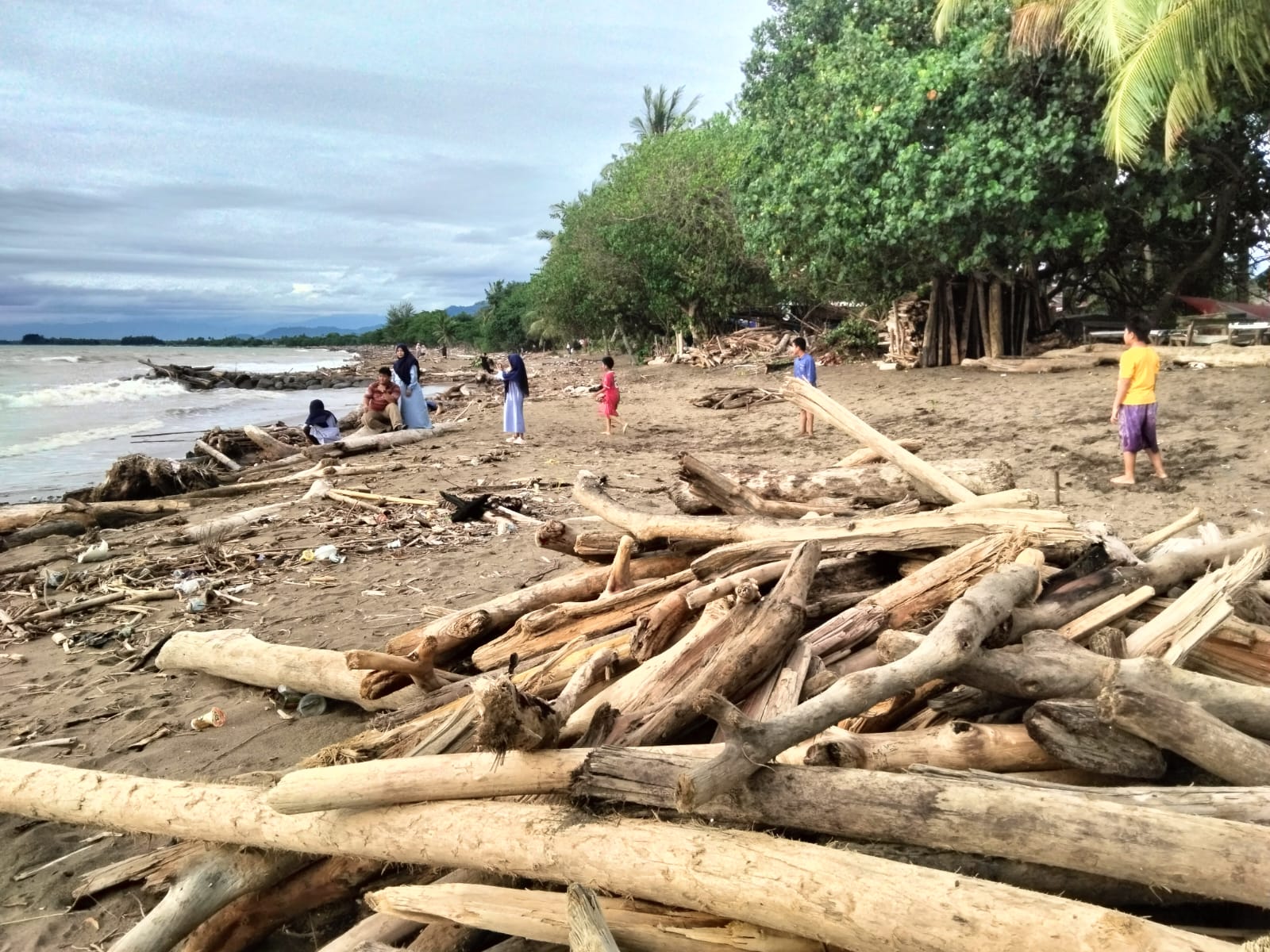 Warga menikmati berwisata di Pantai Parkit Padang yang dipenuhi tumpukan sampah kayu