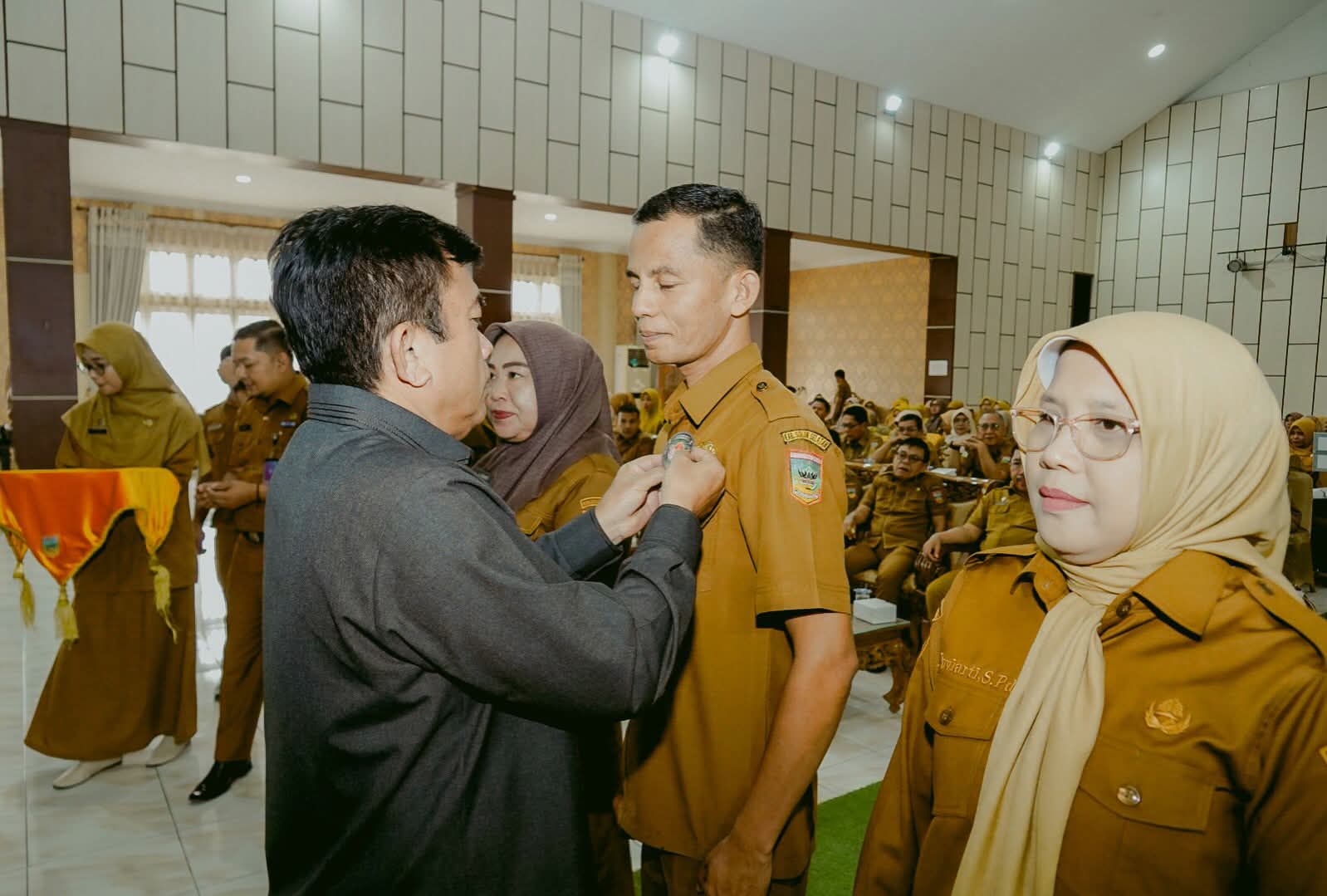 Ketua DPRD Solok Selatan Martius, menyematkan Pin kepada Ketua PGRI Solok Selatan Asbandi, S.Pd., MM pada pembukaan Sosialisasi Anti Korupsi di Aula Sarantau Sasurambi Kantor Bupati Solok Selatan, Senin (19/10/2026). 